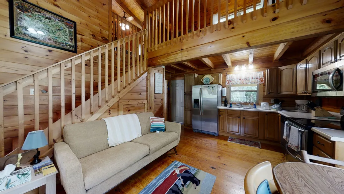 This image highlights the continuity of spaces between the wooden staircase, a plush sofa in the living area, the dining table, and a view of the kitchen beyond. The mood is warm and welcoming, with visible elements like comfortable seating and a backdrop ideal for social or family gatherings.