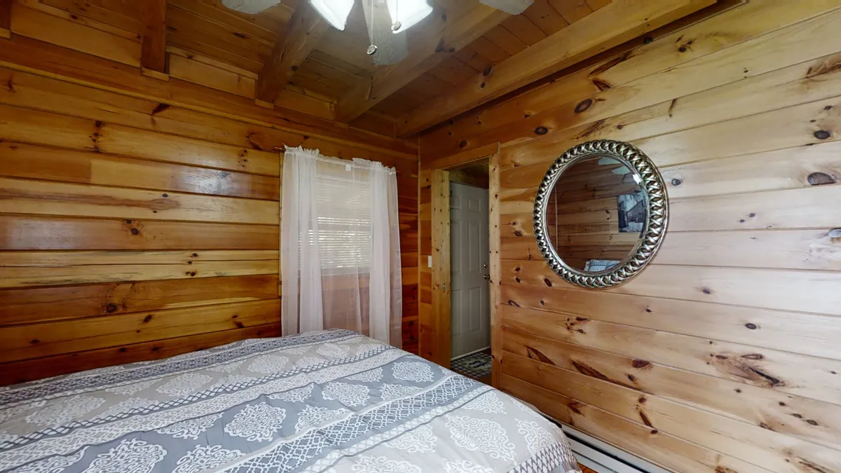An inviting bedroom with wooden walls, a bed adorned in patterned bedding, and a mirror reflecting the room’s gentle lighting. The overall mood is peaceful and warm, suggesting a comfortable spot for couples to unwind and connect.