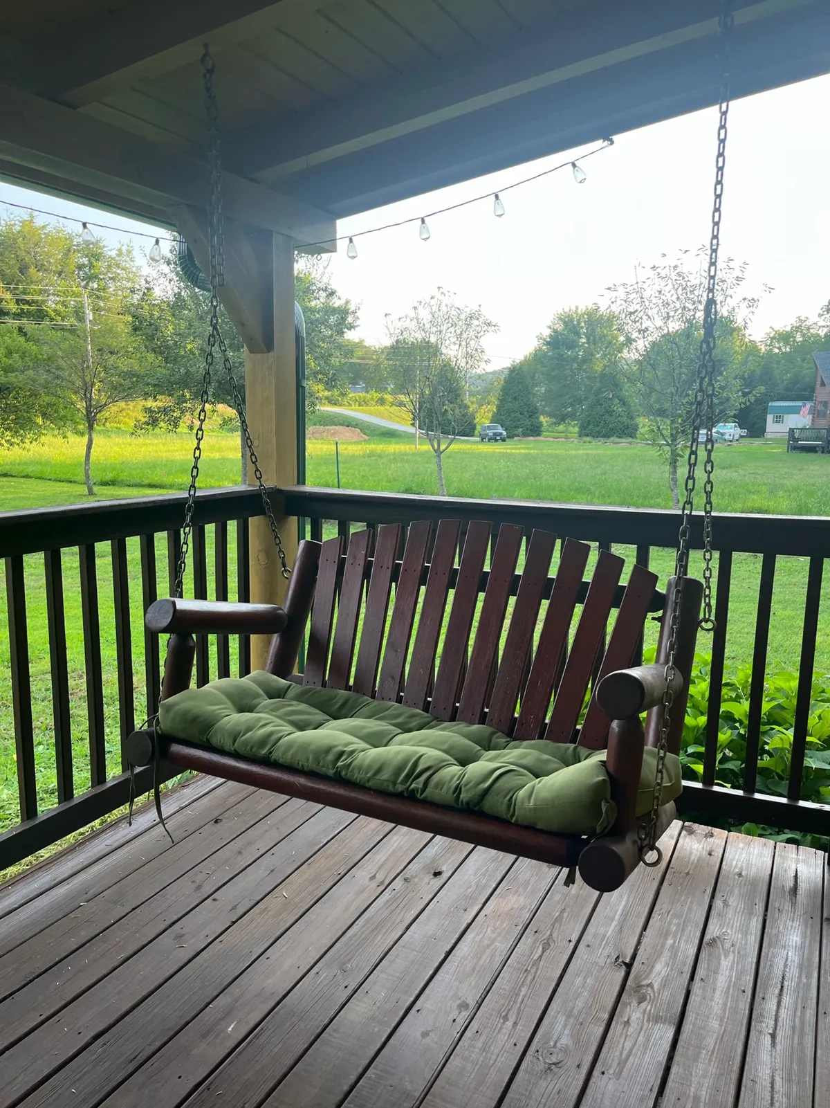 A cozy swing bench with a green cushion is nestled amidst lush greenery. The swing is set in a peaceful corner, perfect for enjoying the natural setting, with surrounding foliage creating a tranquil, private ambiance.